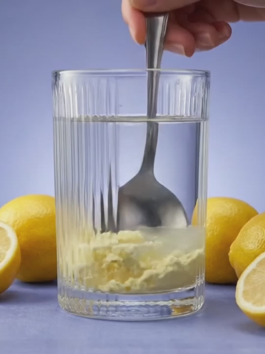Somnii Sleep & energy supplement being stirred in a water glass and turning into a light yellow liquid. The glass in on a light blue background and it is surrounded by lemons