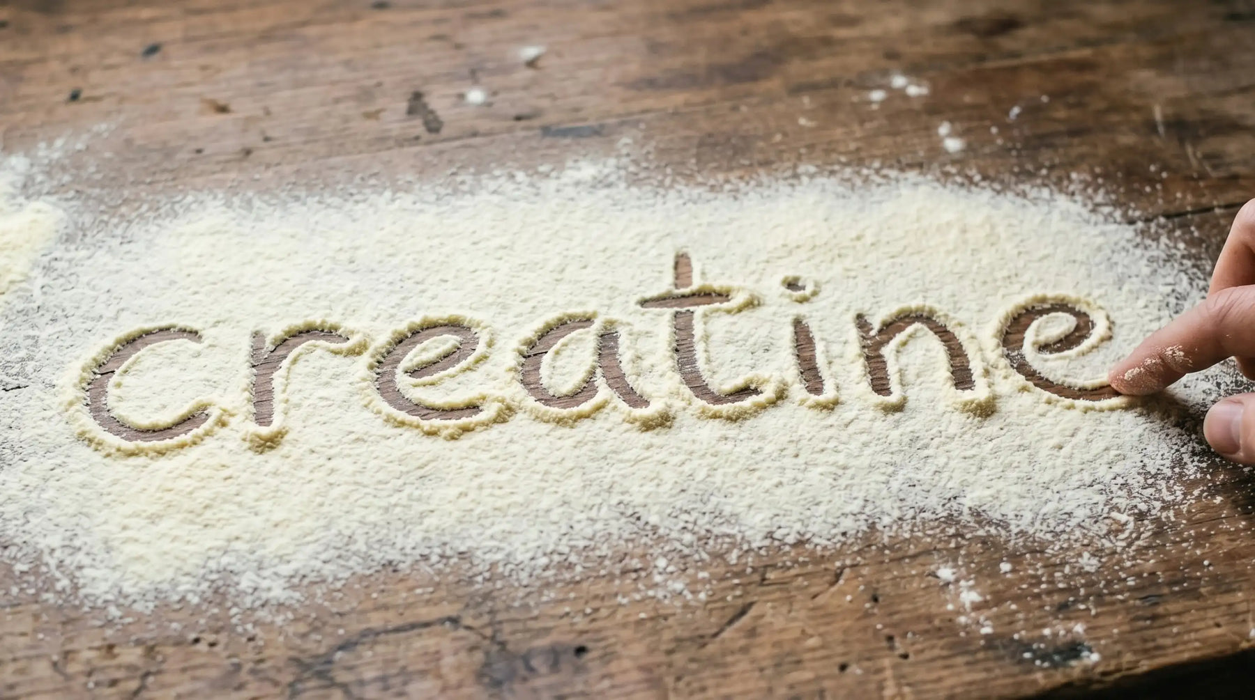 The word 'Creatine' written in white powder on a rustic wooden table, introducing the benefits of creatine monohydrate for maternal brain health and physical energy.