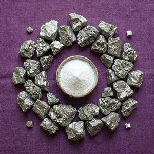 Pure white magnesium powder in a ceramic bowl surrounded by raw magnesium stones on a purple fabric background, representing the high-quality mineral ingredients in Somnii supplements