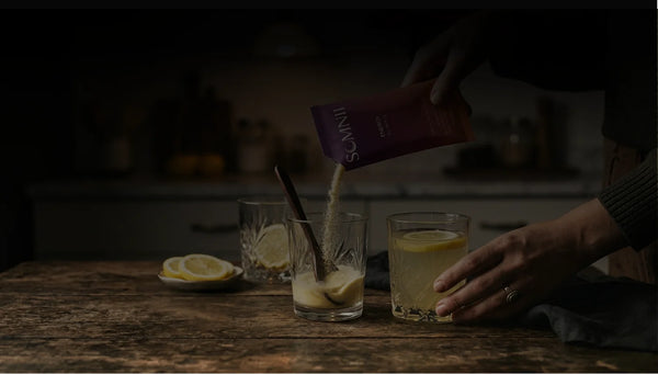 A moody, low-light shot of a mother pouring a Somnii Energy sachet into a glass, highlighting the quiet evening ritual of preparing a clean-ingredient supplement for maternal focus.