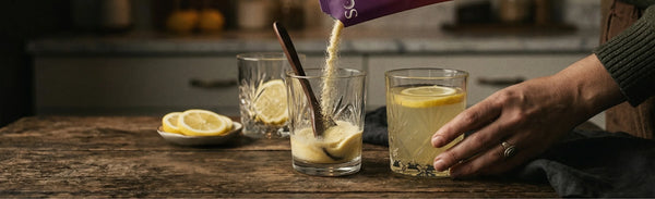 Pouring Somnii magnesium, creatine and l-theanine powder from a purple sachet into a crystal glass with lemon, illustrating the clean and refreshing daily wellness ritual for mothers.