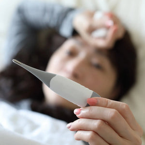 A mother holding a digital thermometer while lying in bed, illustrating how chronic loneliness can impact maternal immunity and physical recovery