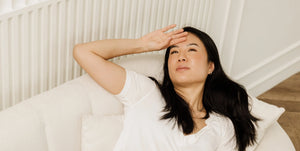 A woman resting on a white sofa with her hand to her forehead, illustrating the burnout of mothers and the long recovery it takes. 