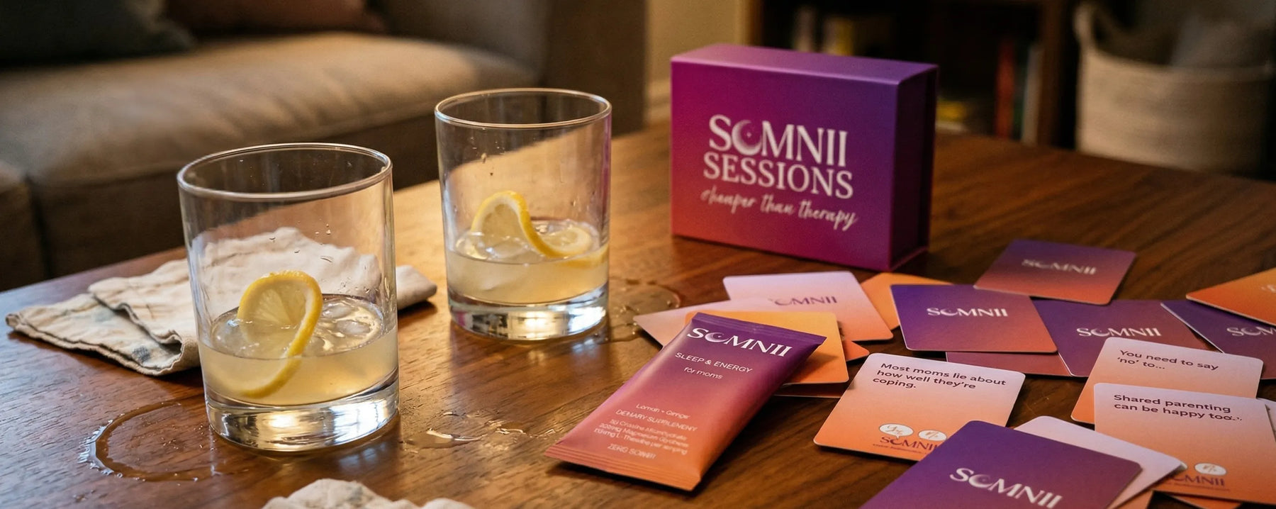 The Somnii wellness ritual: A Somnii Sleep & Energy sachet paired with Somnii Sessions conversation cards on a wooden table with refreshing lemon-infused drinks, representing a holistic approach to maternal mental health