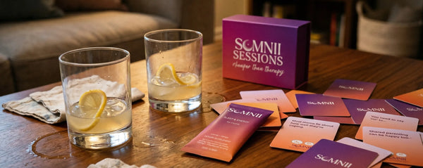 The Somnii wellness ritual: A Somnii Sleep & Energy sachet paired with Somnii Sessions conversation cards on a wooden table with refreshing lemon-infused drinks, representing a holistic approach to maternal mental health
