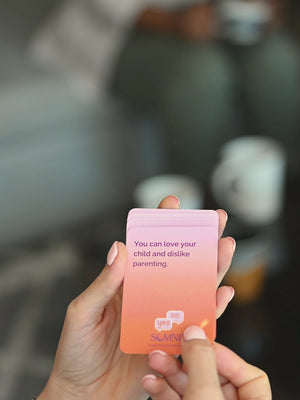 A mom turning a Somnii Says conversation card saying 'you can love your child and dislike parenting. 