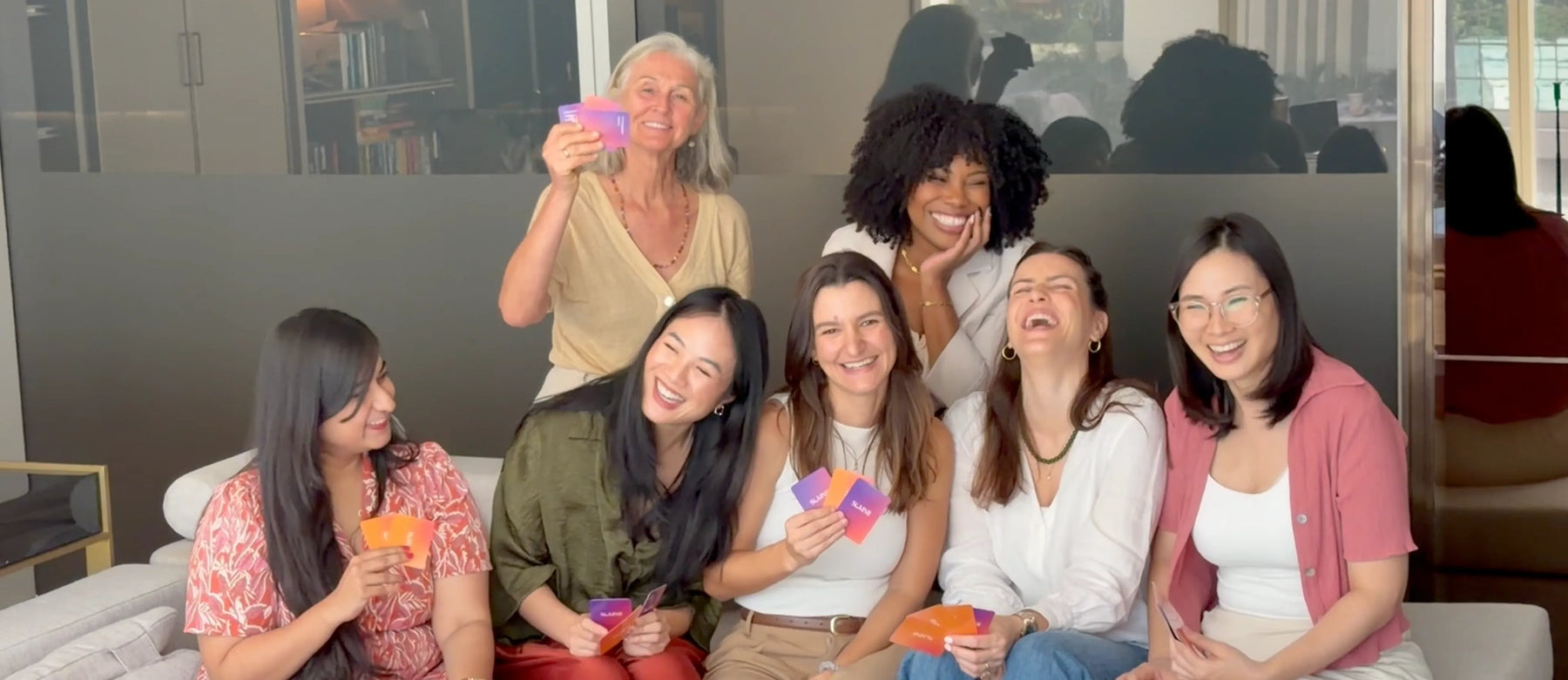 A diverse group of mothers laughing and sharing stories with Somnii Sessions cards, illustrating the power of community and radical honesty in maternal wellness.