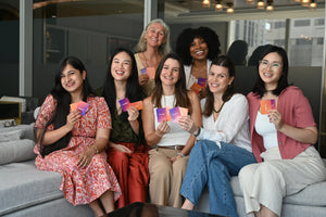A diverse group of smiling moms of various ages and backgrounds holding Somnii Sessions cards, illustrating the shared connection and community supported by Somnii wellness products.
