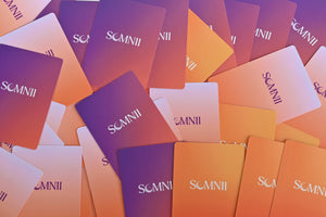 Overhead view of many Somnii brand cards scattered across a surface, showing various shades of purple, pink, and orange gradients with the Somnii logo centered on each.
