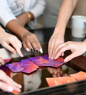 Hands reaching for Somnii Sessions conversation cards spread out on a dark coffee table during a group session for mothers